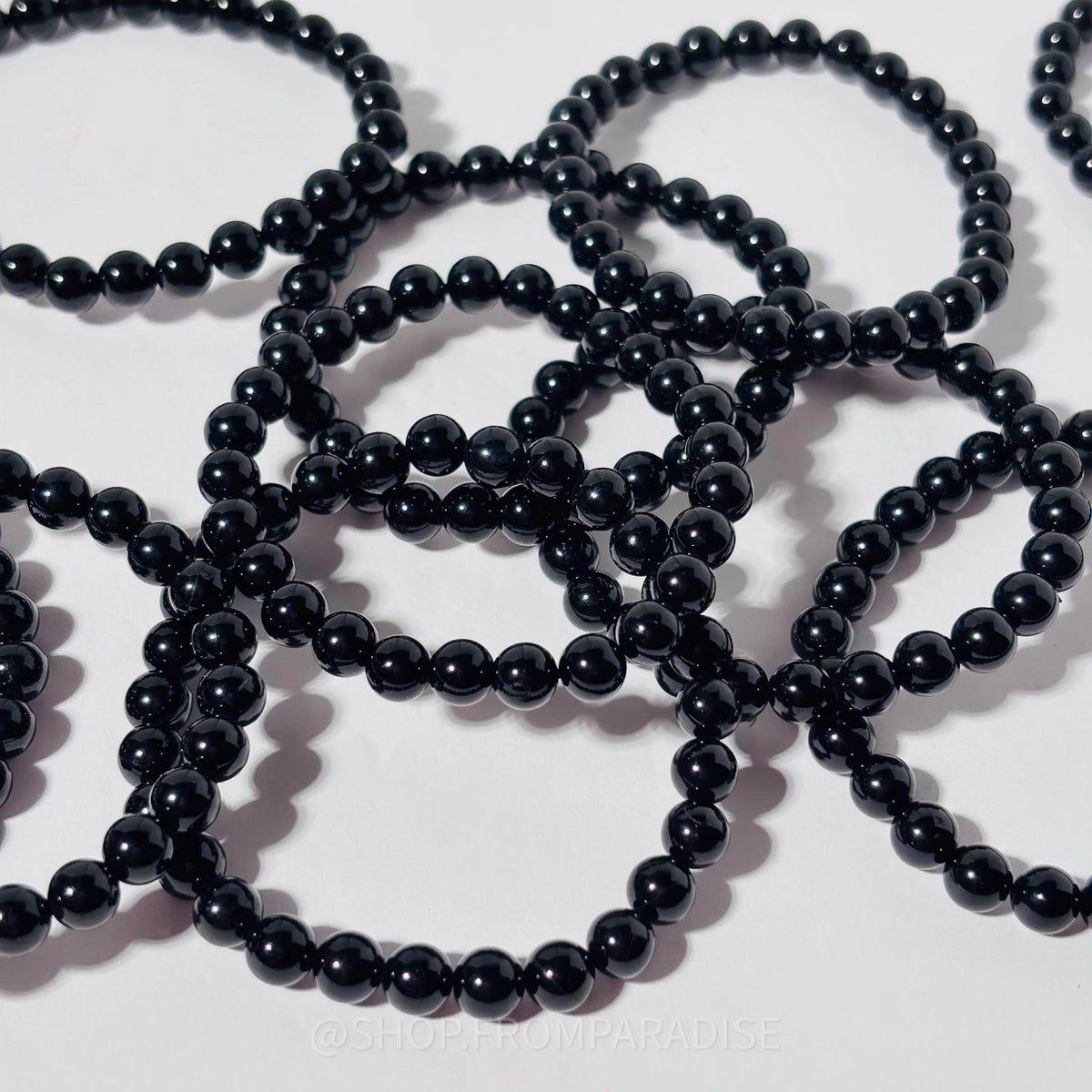 Multiple strands of glossy black round beads arranged in loops on a plain white background.