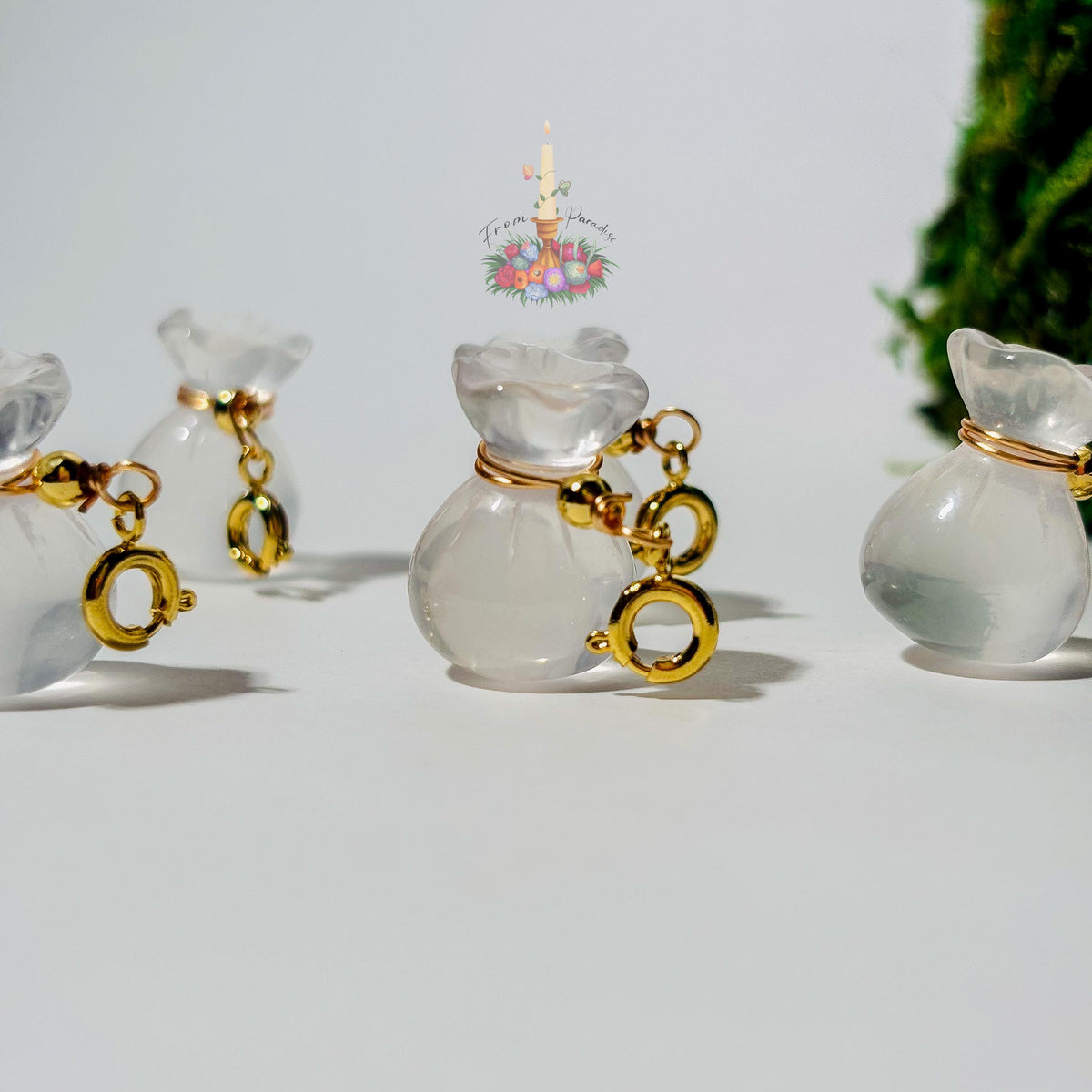 Four mini clear quartz money bag gemstone charms with gold wire wrapping and lobster clasps laid out on a clean white background.