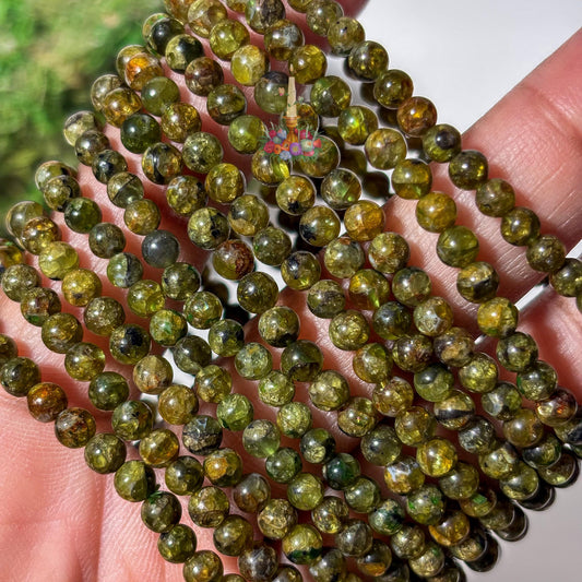 Close-up view of several 4mm genuine peridot beaded stretch bracelets held across a hand, showcasing the detailed patterns, inclusions, and natural variations in the round olive green gemstone beads.