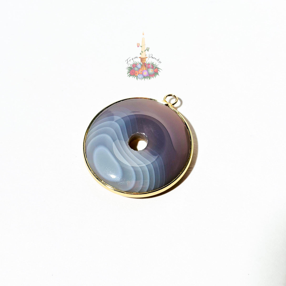 A round pendant with a central hole, featuring a marbled agate pattern in shades of purple, gray, and blue, set in a gold-toned bezel with a small hanging loop at the top, shown on a white background.