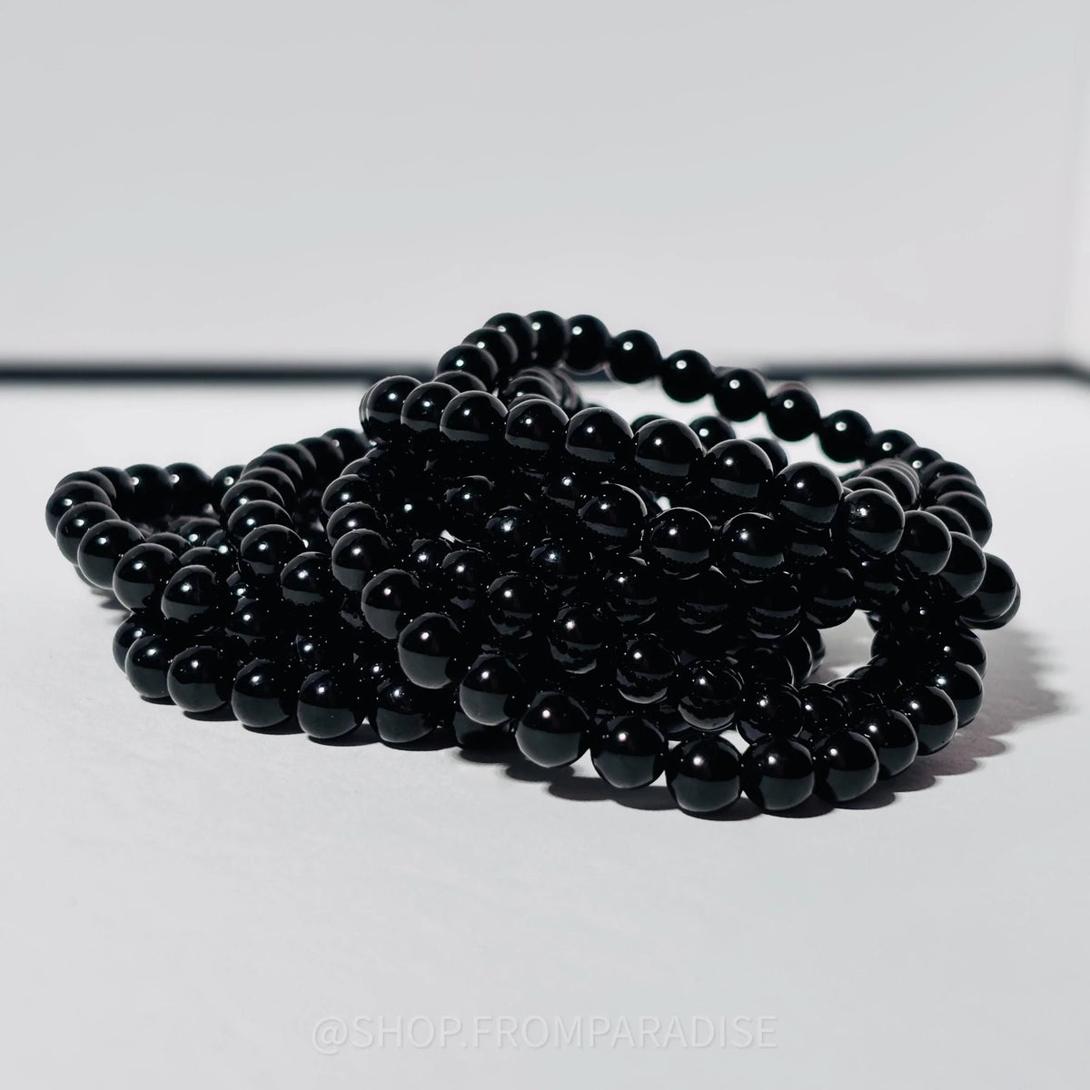 A coiled stack of glossy black round beads, likely for jewelry making, photographed on a light gray background.