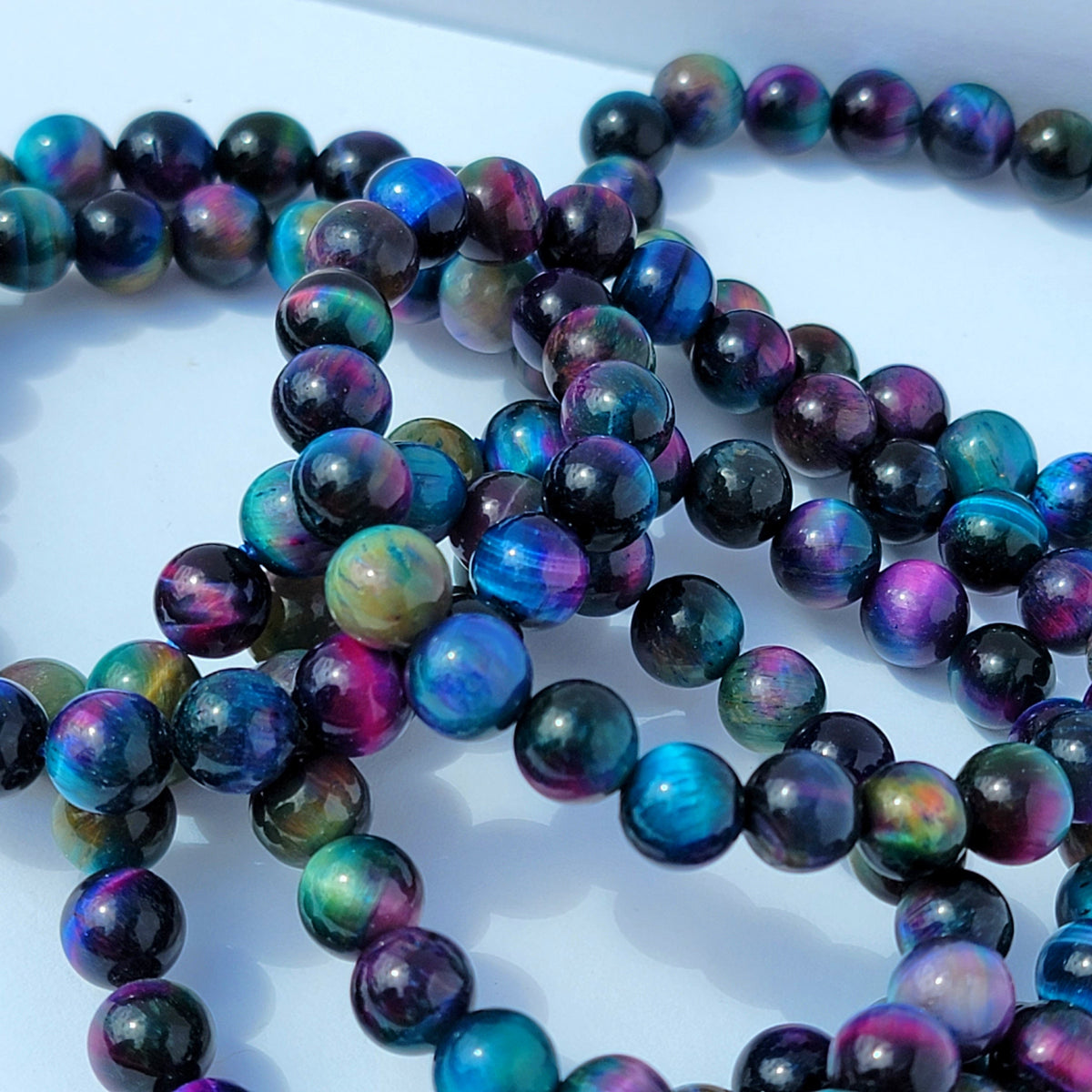 Close-up of iridescent round beads with a black base and vivid blue, purple, green, and pink flashes, arranged on a white surface.