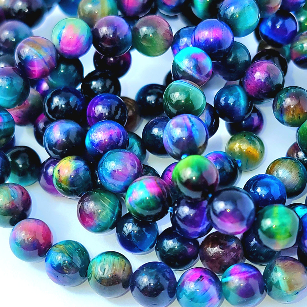 A close-up pile of round iridescent beads with swirling colors of blue, purple, green, pink, and black on a white background.