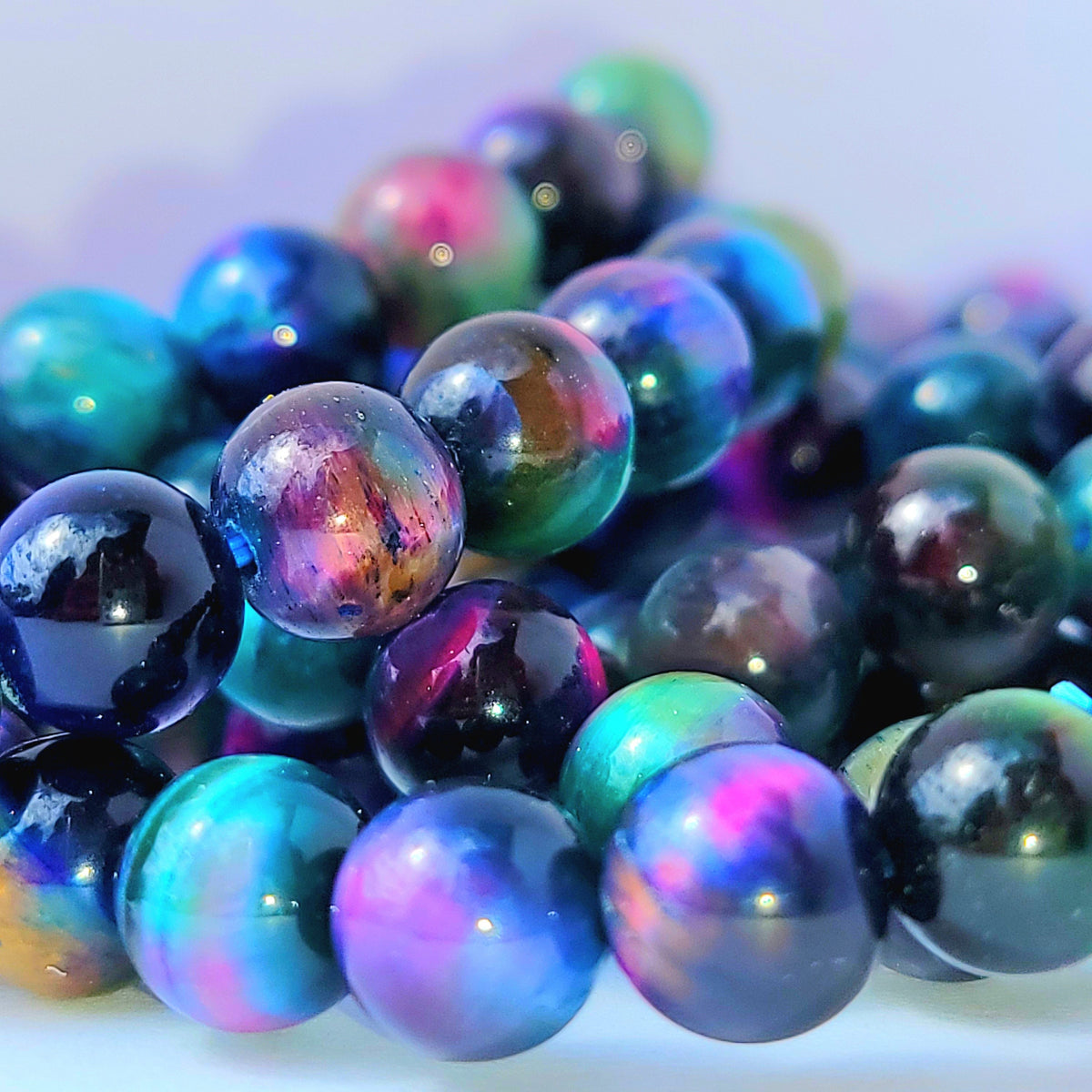 Close-up of glossy iridescent beads with a galaxy-like color shift between blue, purple, teal, and pink on a soft light background.