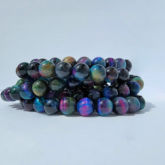 A stack of iridescent beaded bracelets made of round dark beads that shift between blue, purple, green, and pink, photographed on a clean light gray background.
