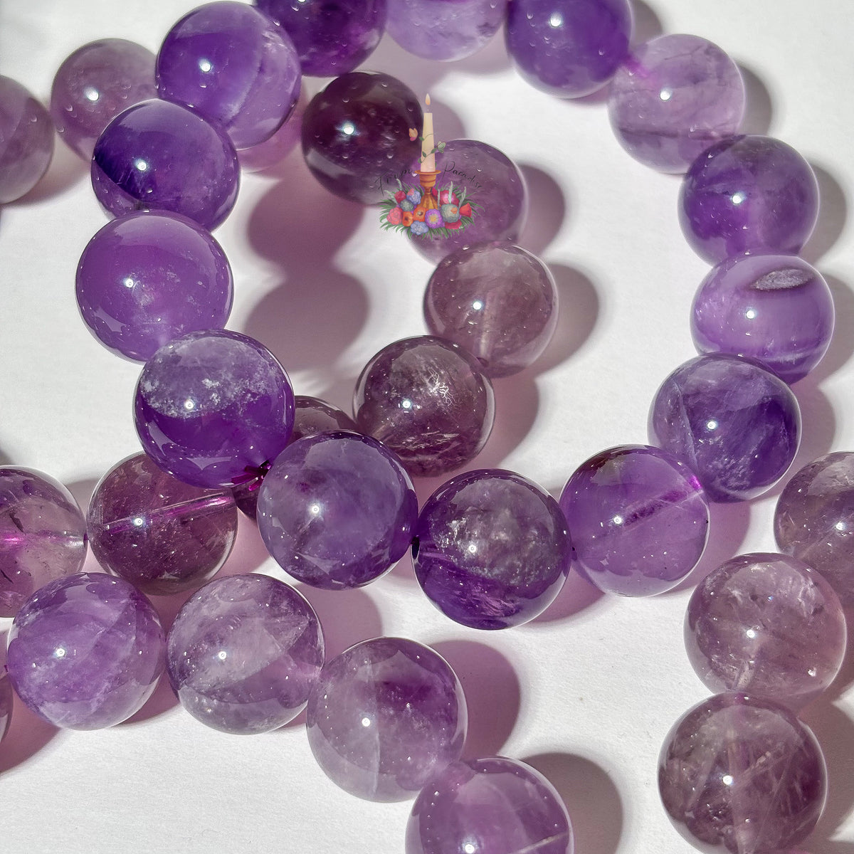 Purple amethyst gemstone beads arranged in a circle on a white background, showing natural inclusions and polished round spheres.