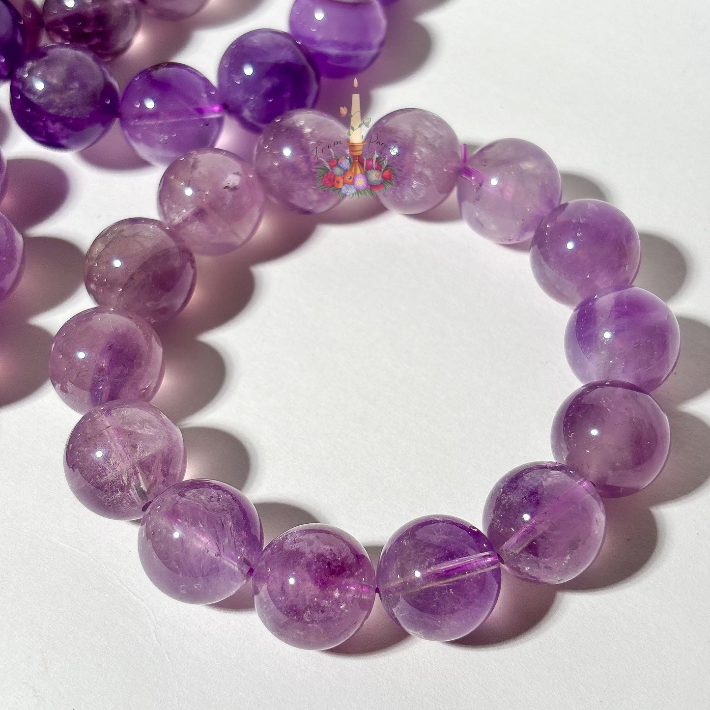 A purple amethyst beaded bracelet made of polished round beads, shown on a white surface with other similar bracelets partially visible in the background.
