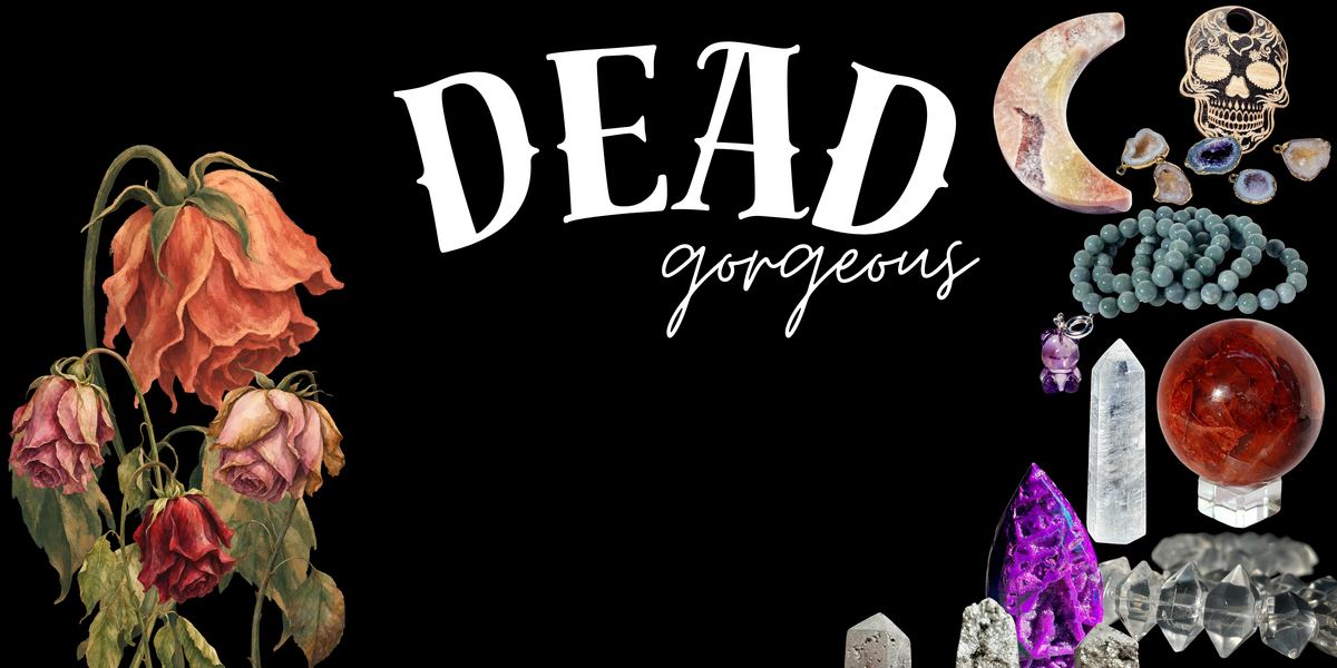 A black graphic banner with the words 'DEAD gorgeous' in large white lettering, surrounded by gothic decorative items including dried roses, crystals, a skull, beads, and a red orb.