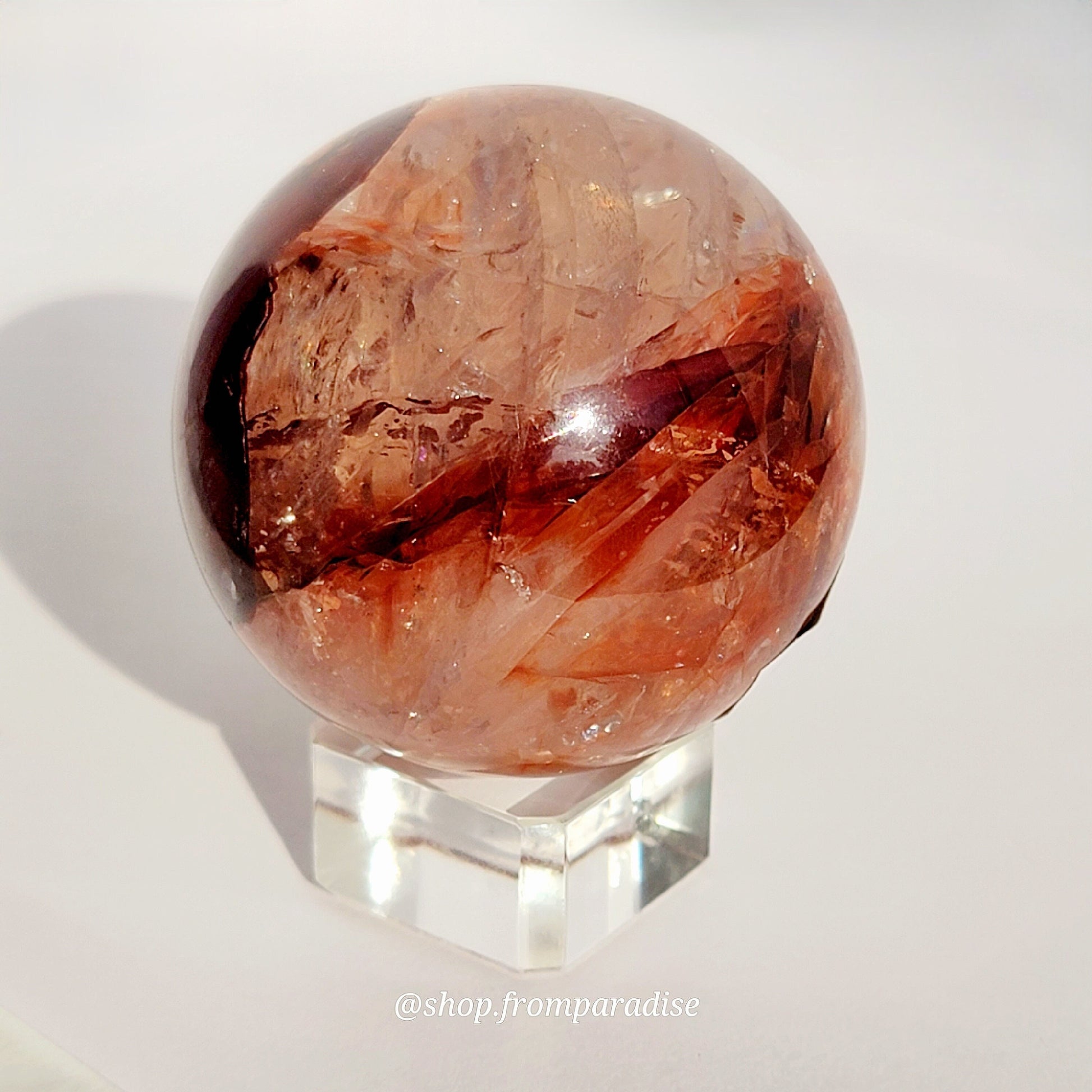 Fire Quartz Red Hematoid Sphere against white background on glass sphere holder