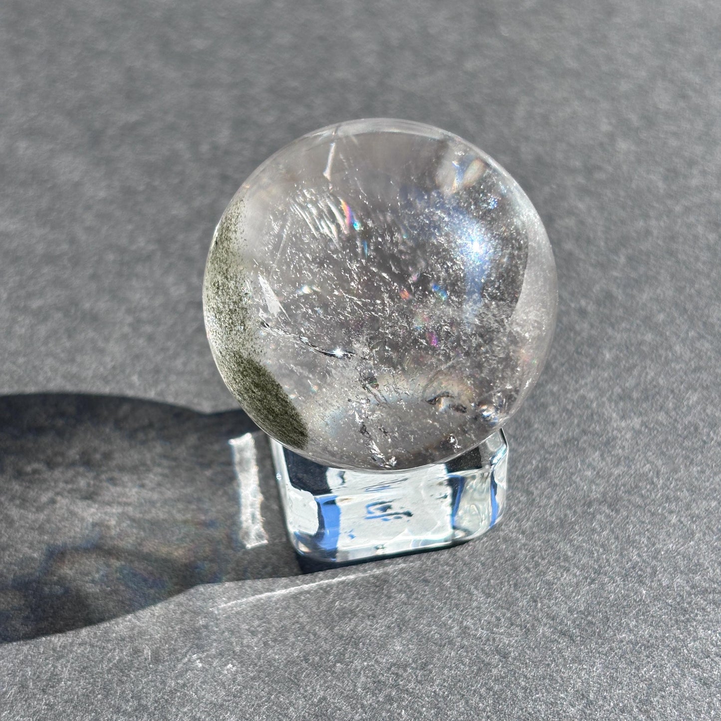 Clear Quartz with Chloride Crystal Sphere against a black background on a glass sphere holder