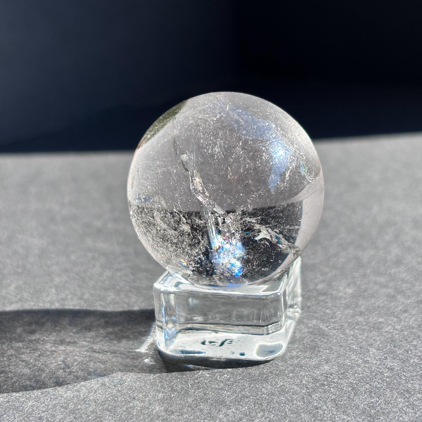 Clear Quartz with Chloride Crystal Sphere against a black background on a glass sphere holder