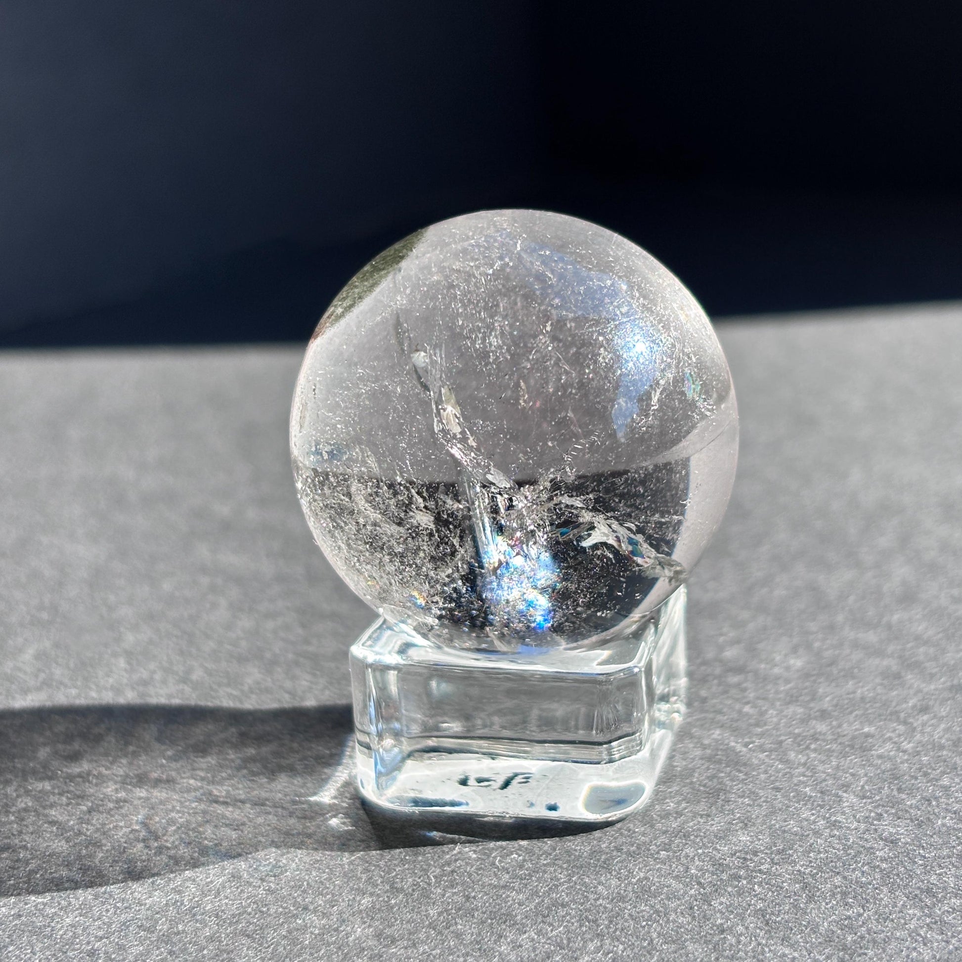 Clear Quartz with Chloride Crystal Sphere against a black background on a glass sphere holder