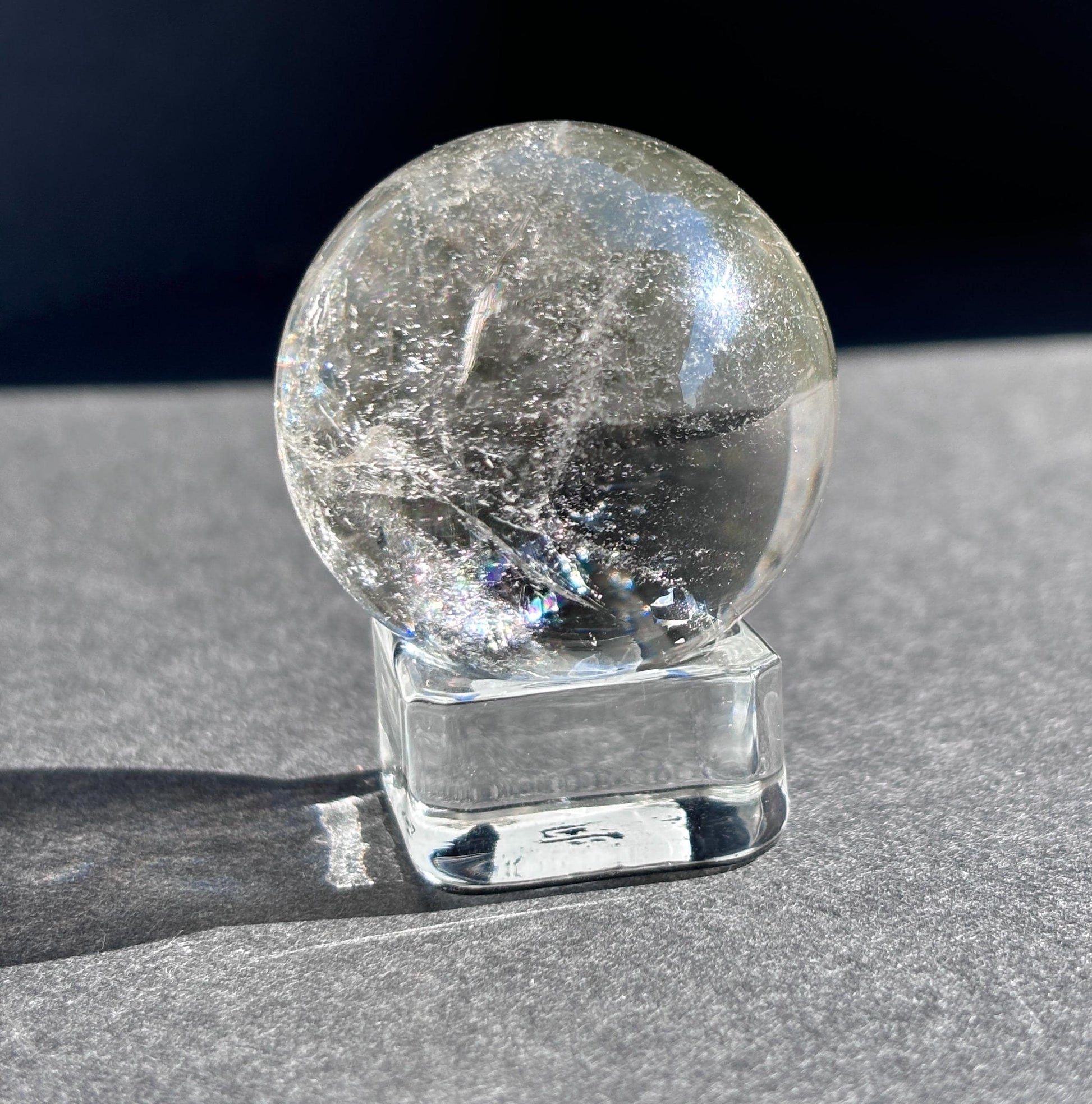 Clear Quartz with Chloride Crystal Sphere against a black background on a glass sphere holder