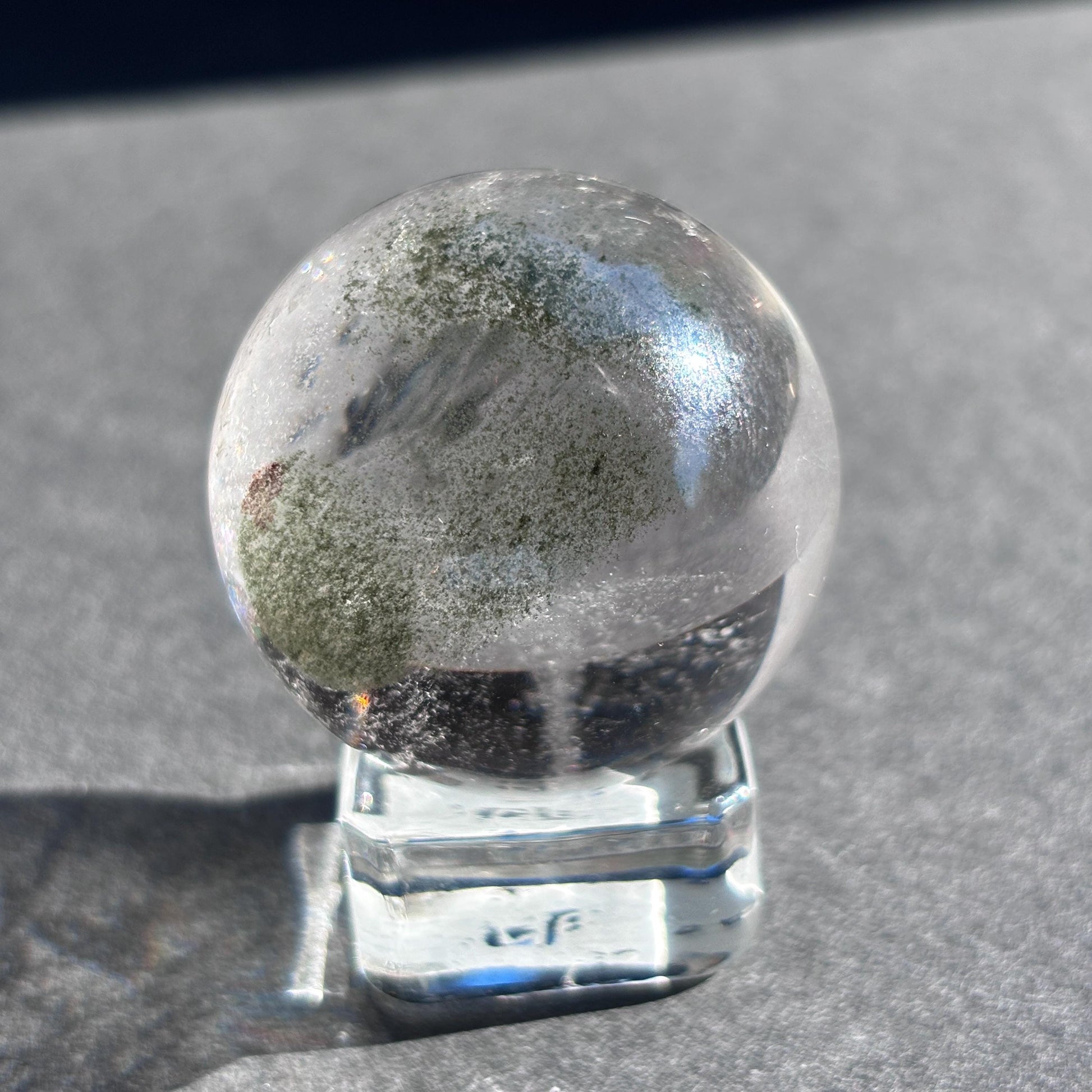 Clear Quartz with Chloride Crystal Sphere against a black background on a glass sphere holder