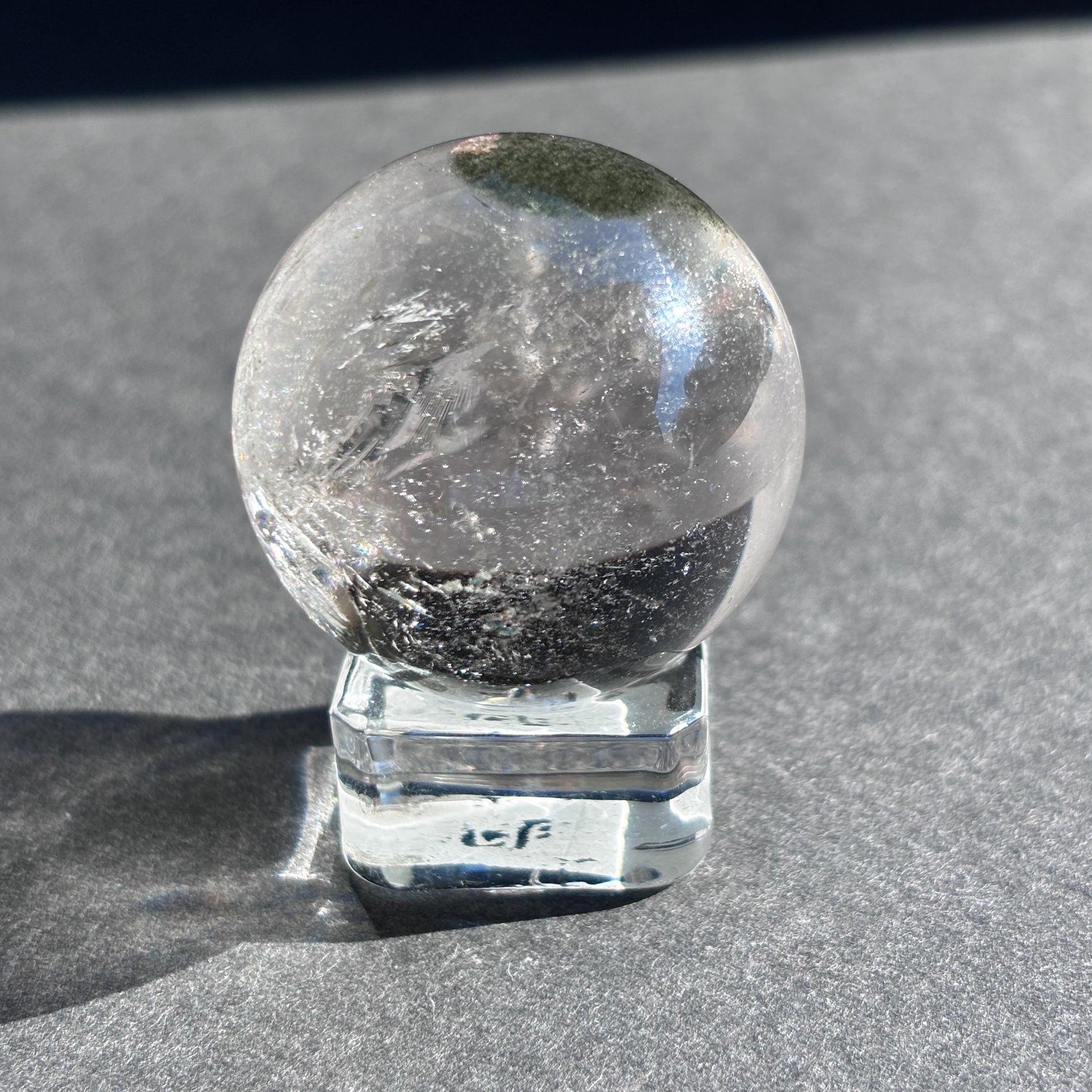 Clear Quartz with Chloride Crystal Sphere against a black background on a glass sphere holder