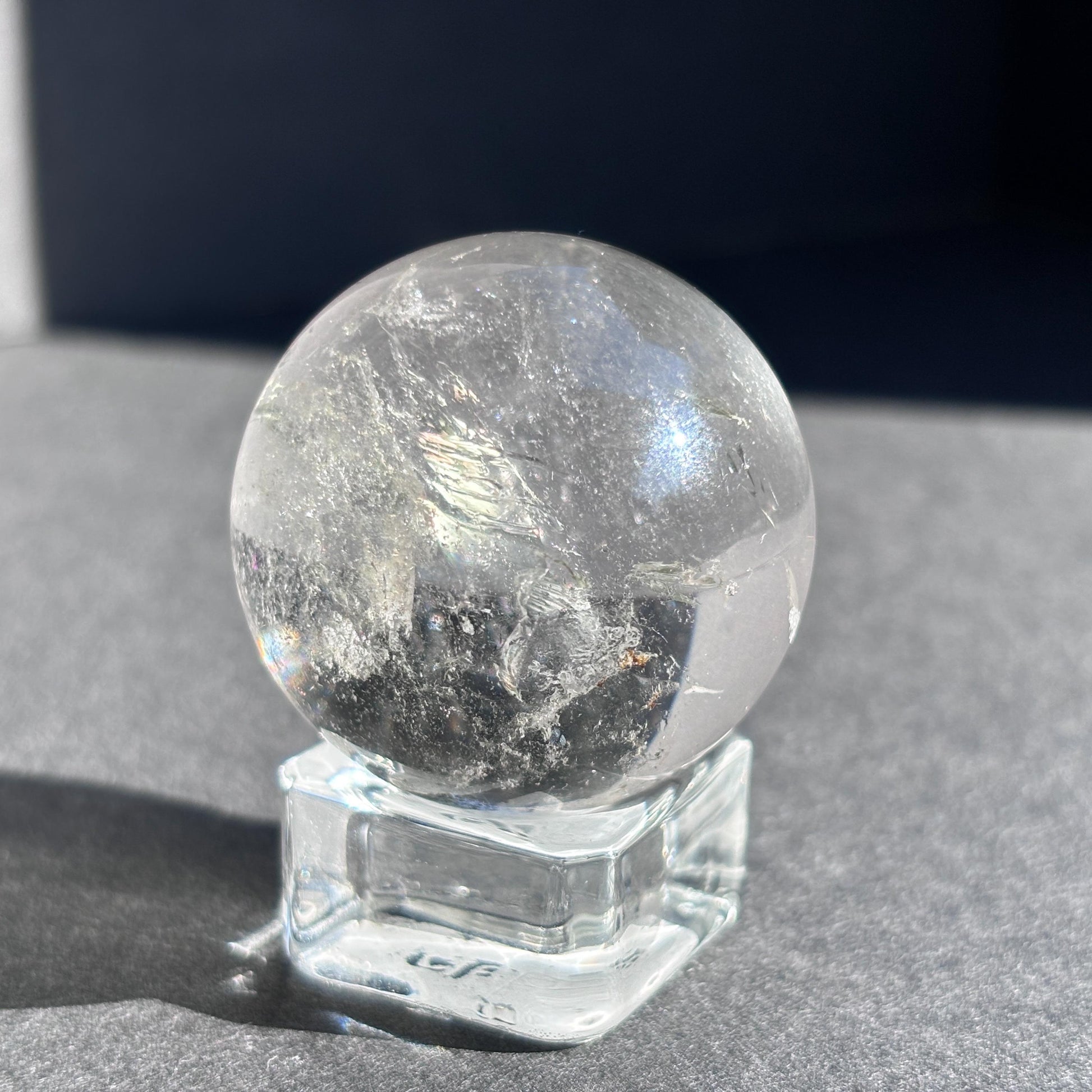 Clear Quartz with Chloride Crystal Sphere against a black background on a glass sphere holder