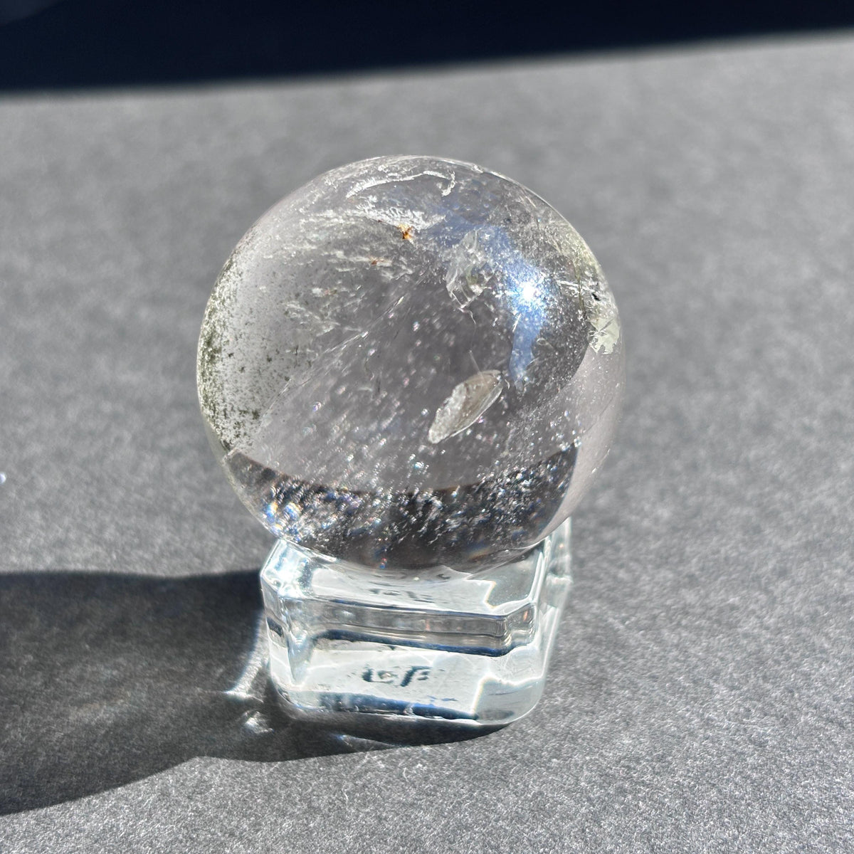 Clear Quartz with Chloride Crystal Sphere against a black background on a glass sphere holder