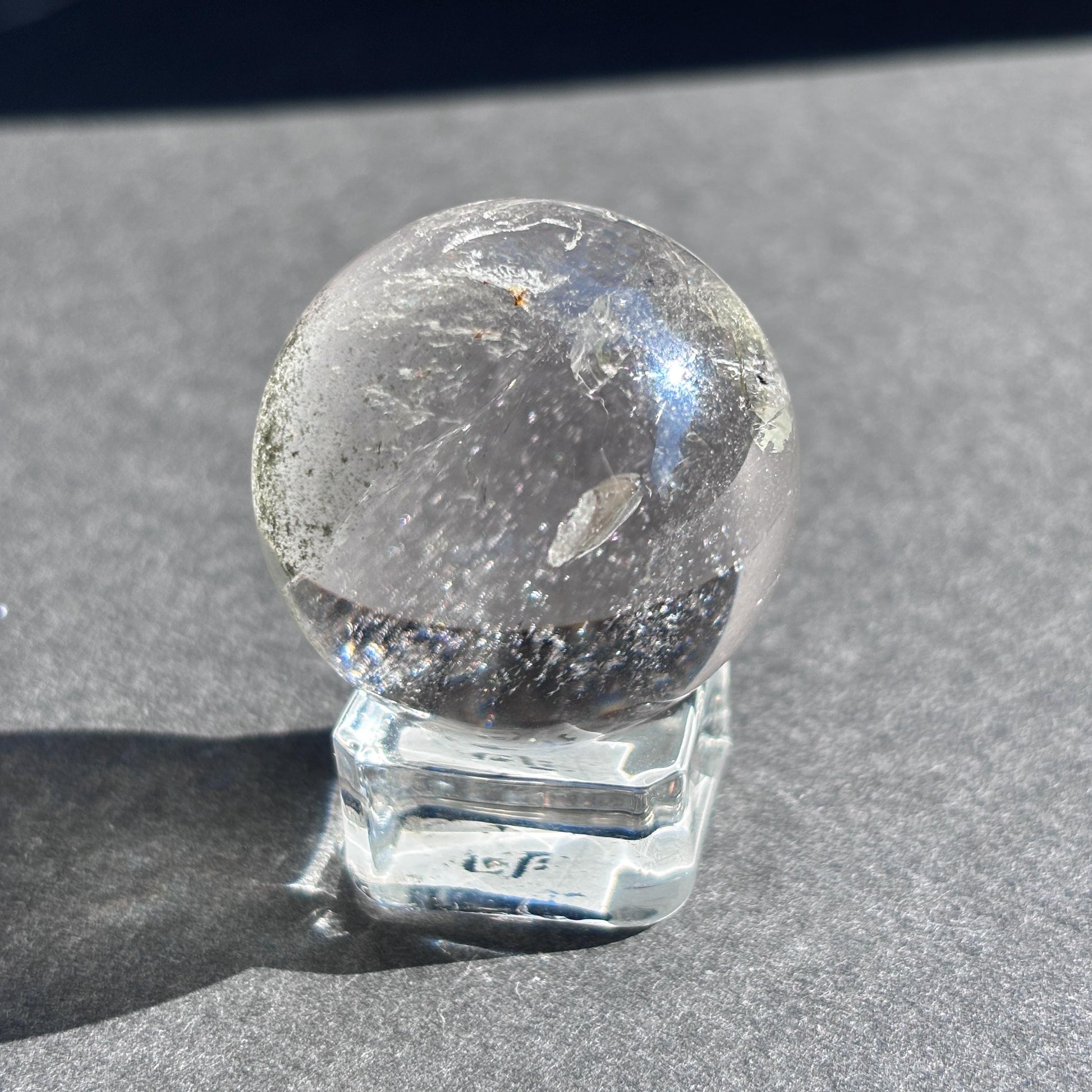 Clear Quartz with Chloride Crystal Sphere against a black background on a glass sphere holder