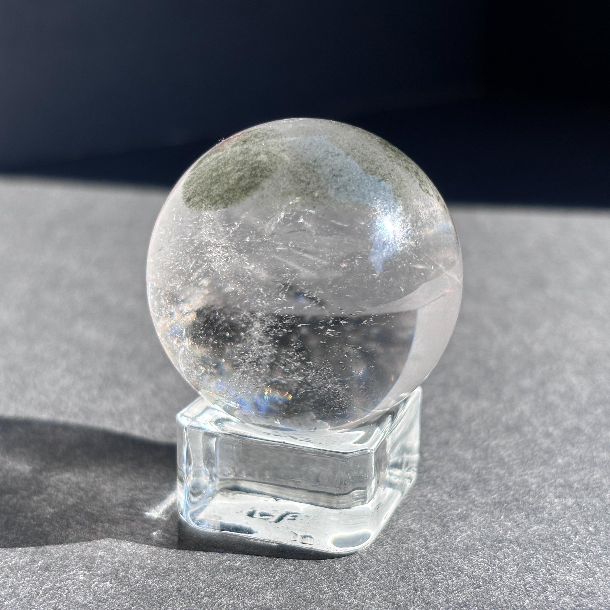 Clear Quartz with Chloride Crystal Sphere against a black background on a glass sphere holder