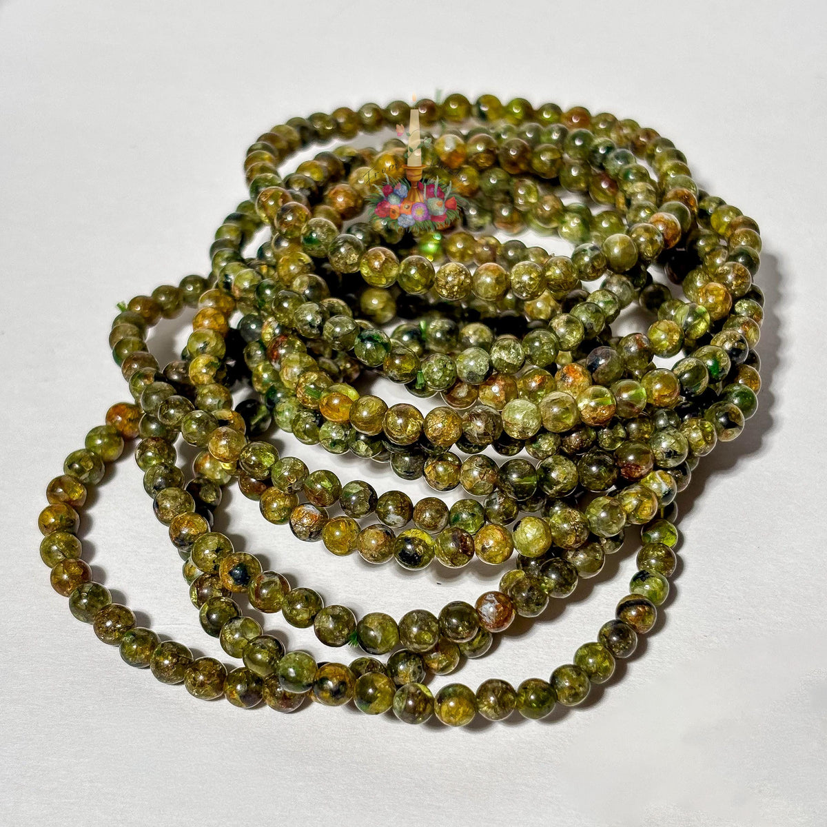 A stacked pile of handmade 4mm genuine peridot beaded stretch bracelets featuring small round olive green gemstone beads on a plain white background.
