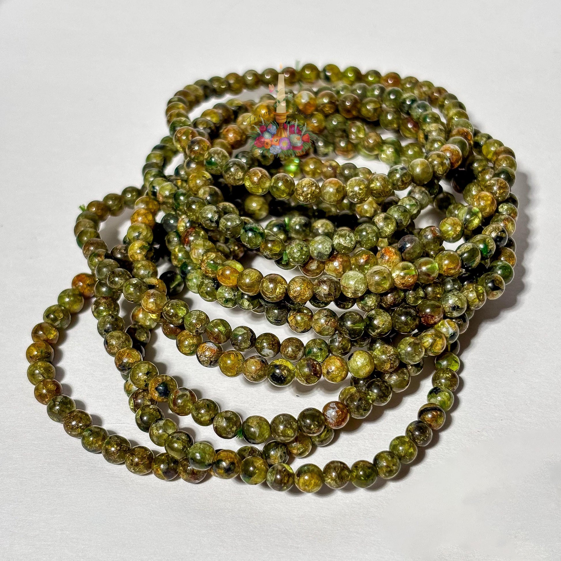 A stacked pile of handmade 4mm genuine peridot beaded stretch bracelets featuring small round olive green gemstone beads on a plain white background.