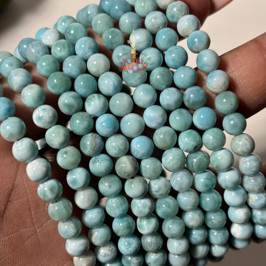 Close-up view of natural Larimar beaded stretch bracelets held in a hand, displaying smooth, polished round beads with light blue and white ocean-like marbling.