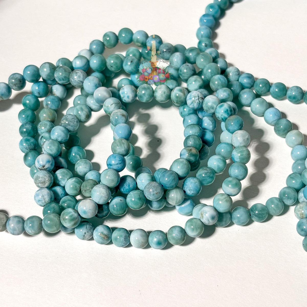 Stack of natural light blue and white Larimar beaded stretch bracelets on a white background, highlighting the gemstone's ocean-like patterns.
