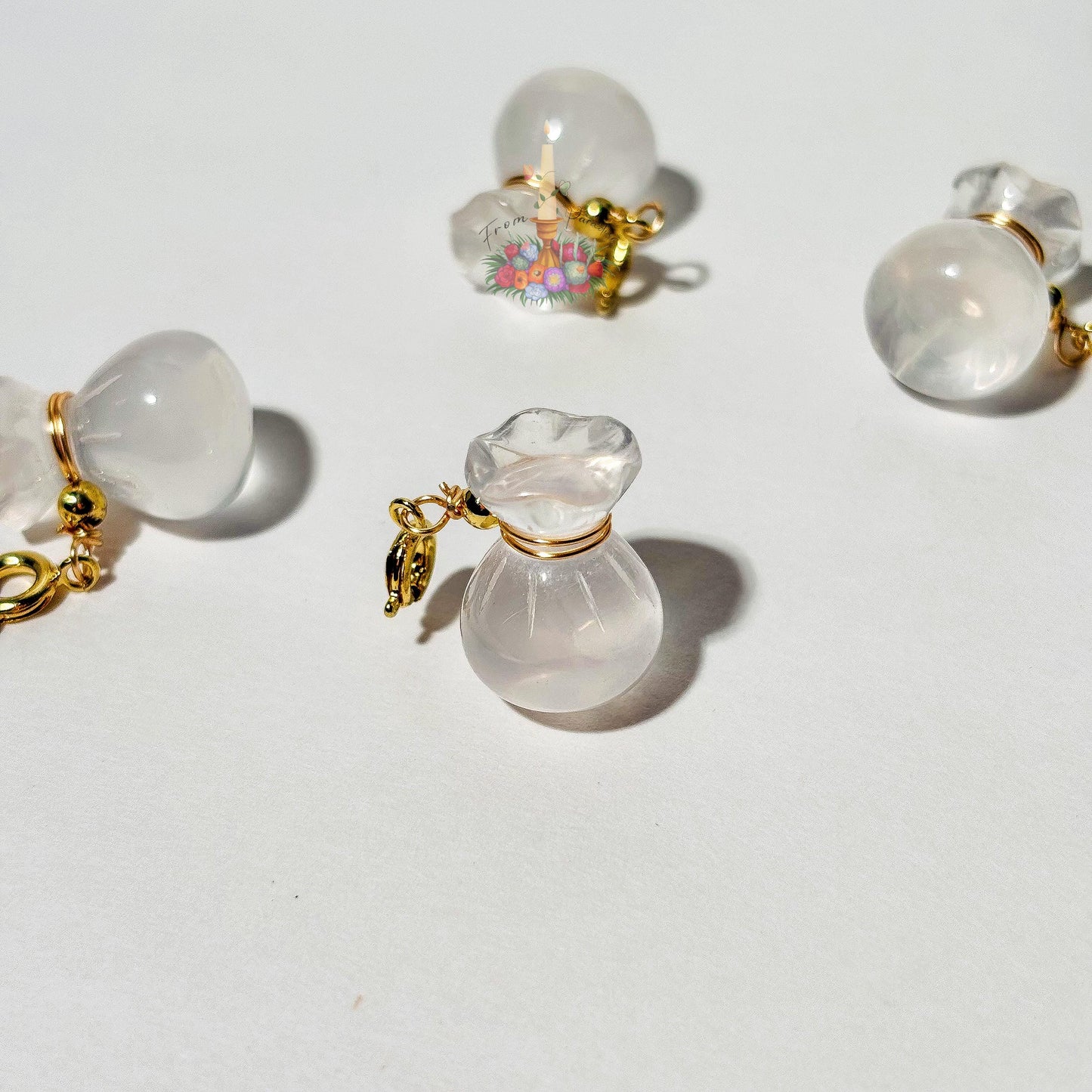 Four mini clear quartz money bag gemstone charms with gold wire wrapping and lobster clasps laid out on a clean white background.