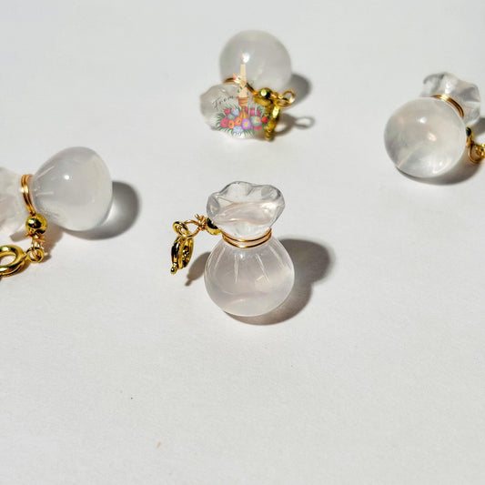 Four mini clear quartz money bag gemstone charms with gold wire wrapping and lobster clasps laid out on a clean white background.