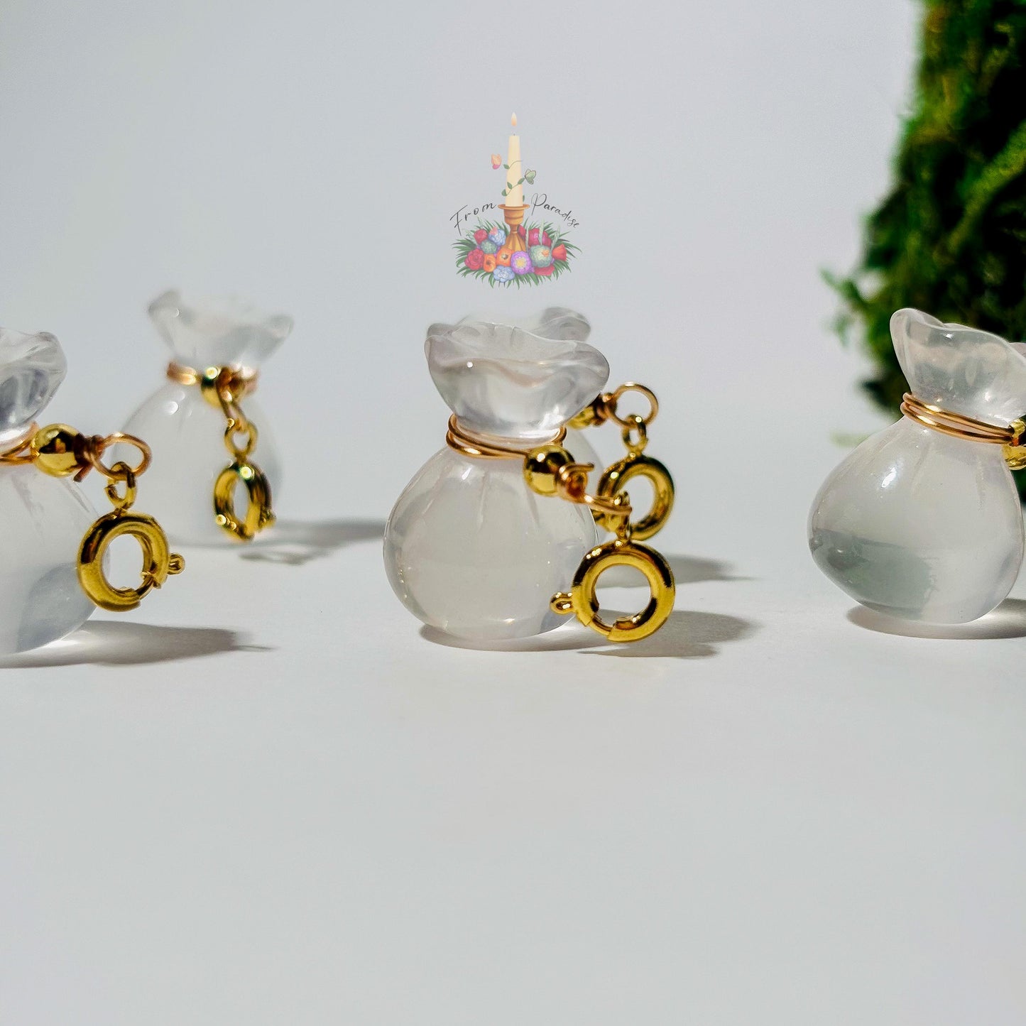 Four mini clear quartz money bag gemstone charms with gold wire wrapping and lobster clasps laid out on a clean white background.