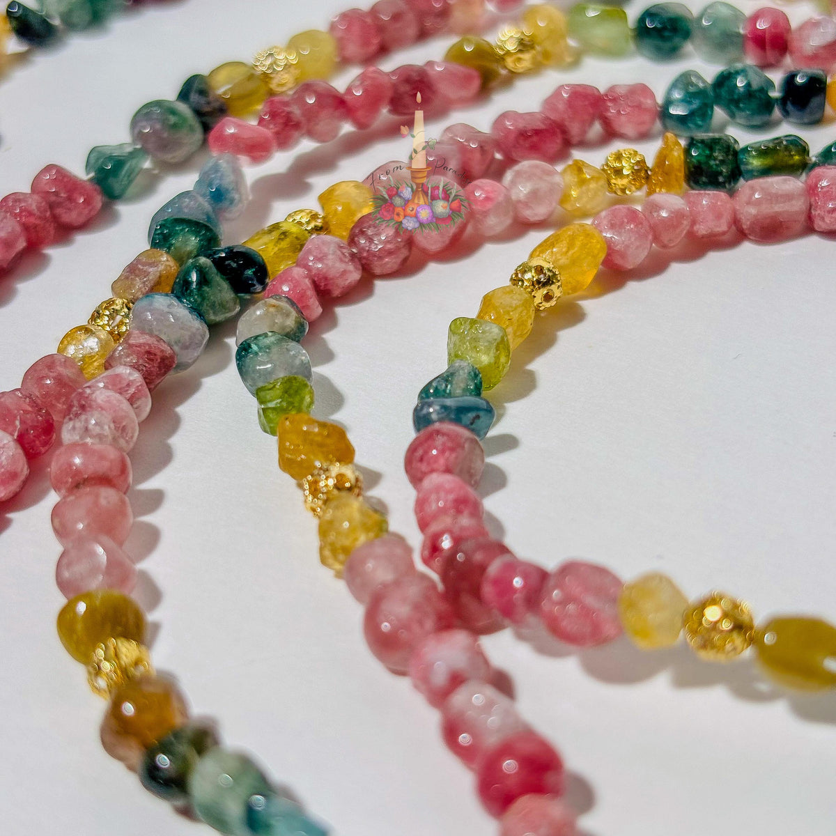 Macro close-up photograph showcasing the translucency and natural texture of multi-colored tourmaline gemstone beads and textured gold accent beads.
