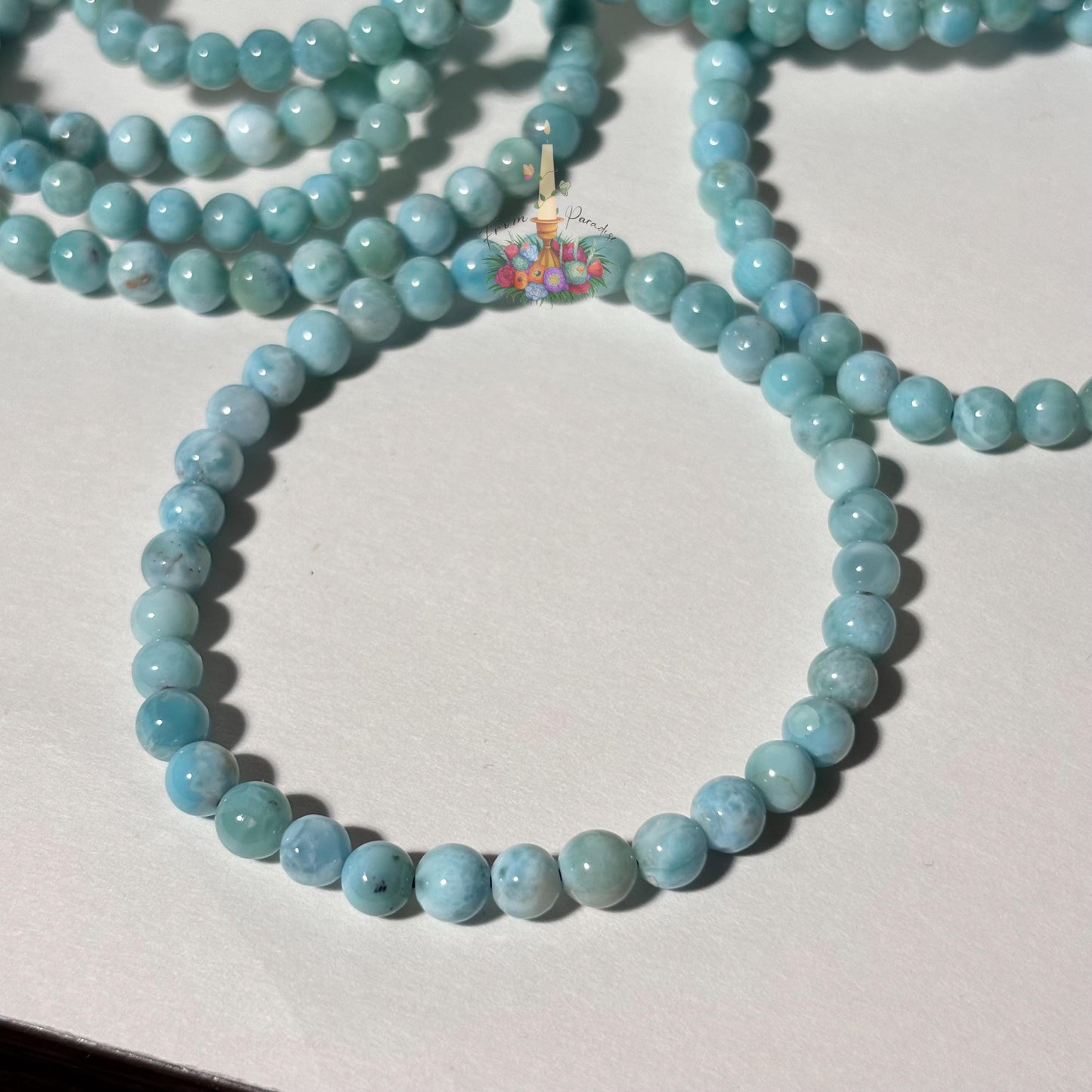 Stack of natural light blue and white Larimar beaded stretch bracelets on a white background, highlighting the gemstone's ocean-like patterns.