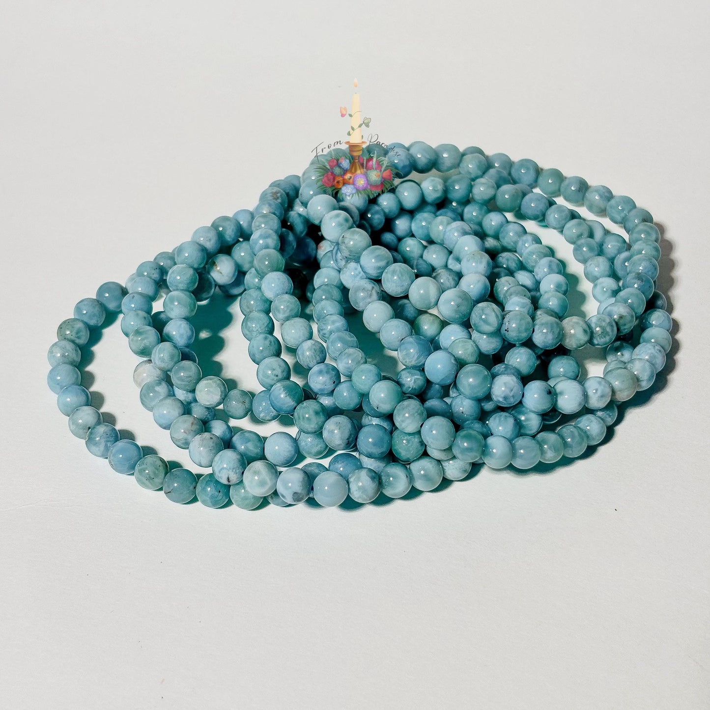 Stack of natural light blue and white Larimar beaded stretch bracelets on a white background, highlighting the gemstone's ocean-like patterns.