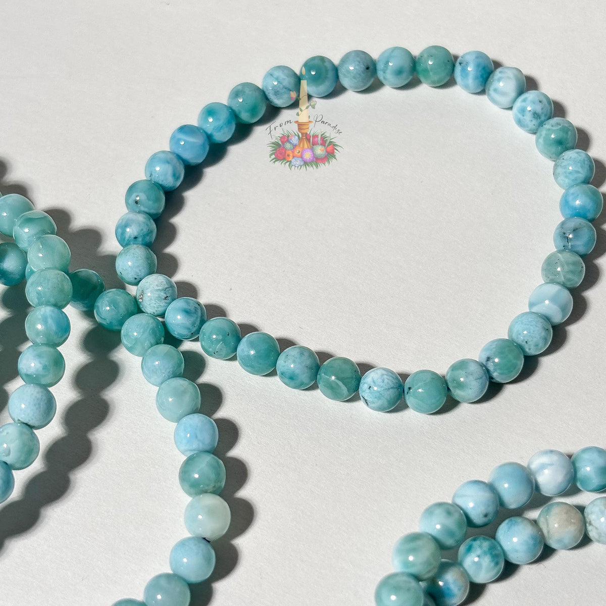 Stack of natural light blue and white Larimar beaded stretch bracelets on a white background, highlighting the gemstone's ocean-like patterns.