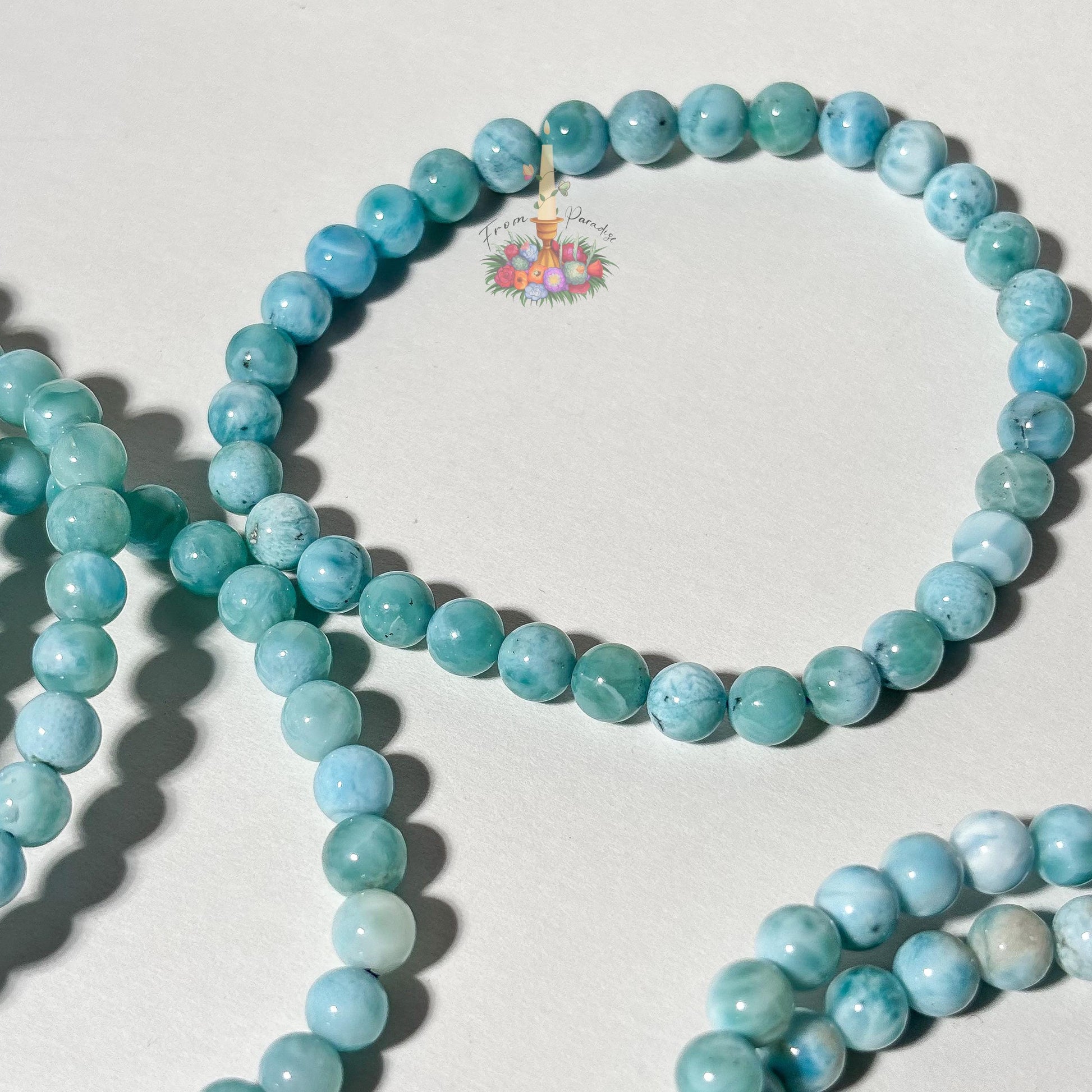 Stack of natural light blue and white Larimar beaded stretch bracelets on a white background, highlighting the gemstone's ocean-like patterns.