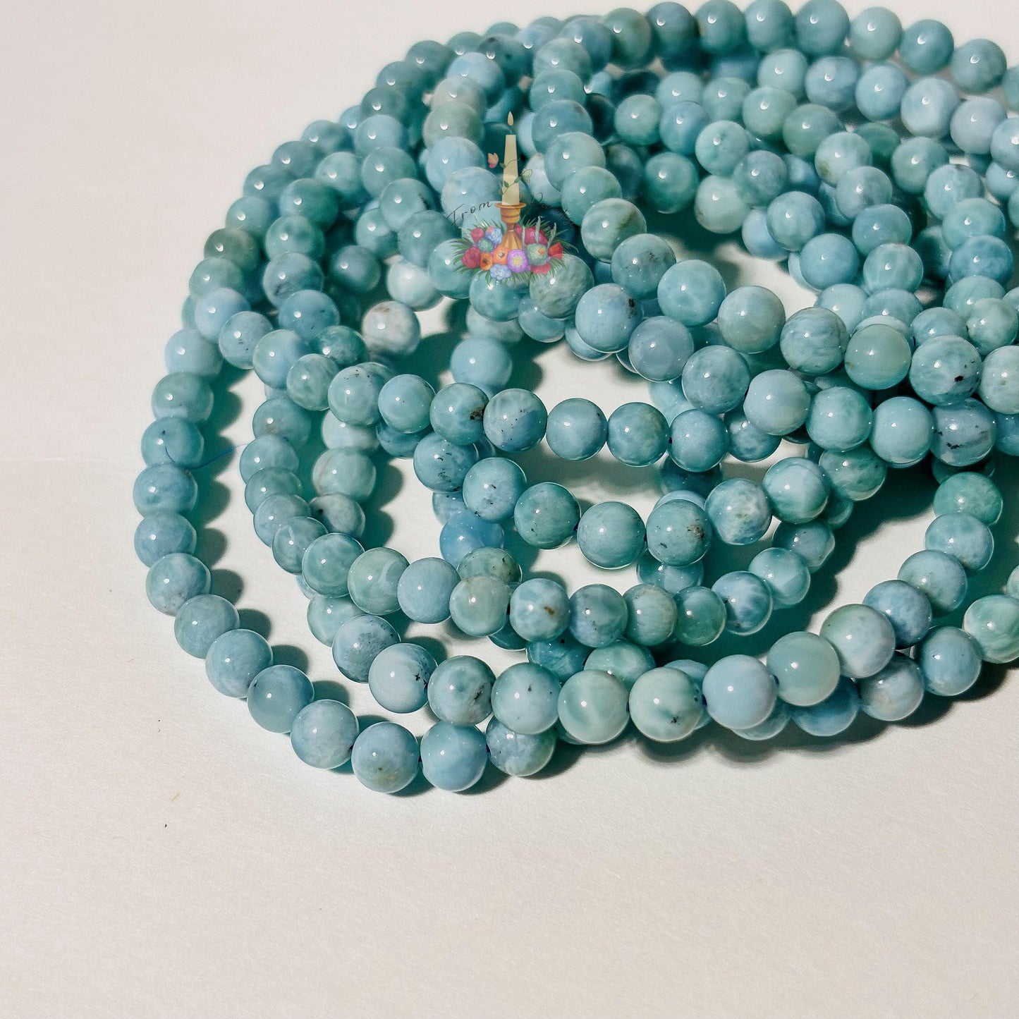 Stack of natural light blue and white Larimar beaded stretch bracelets on a white background, highlighting the gemstone's ocean-like patterns.