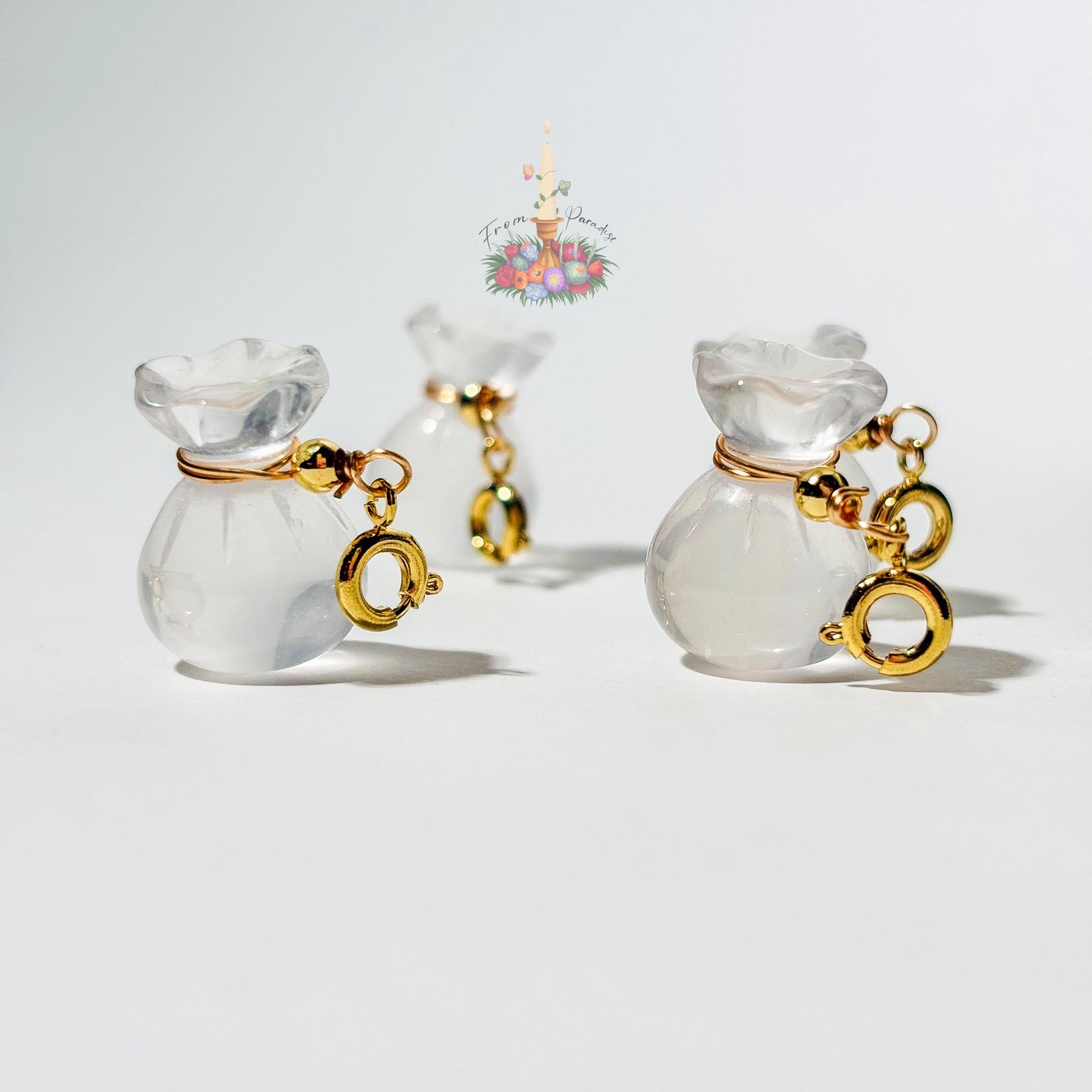 Four mini clear quartz money bag gemstone charms with gold wire wrapping and lobster clasps laid out on a clean white background.